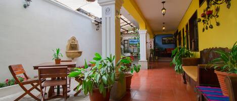A covered patio area with a table and chairs, potted plants, and hanging plants.