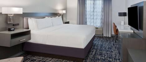 A modern hotel room with a large bed, bedside tables, a flat-screen TV, a desk, and a chair.