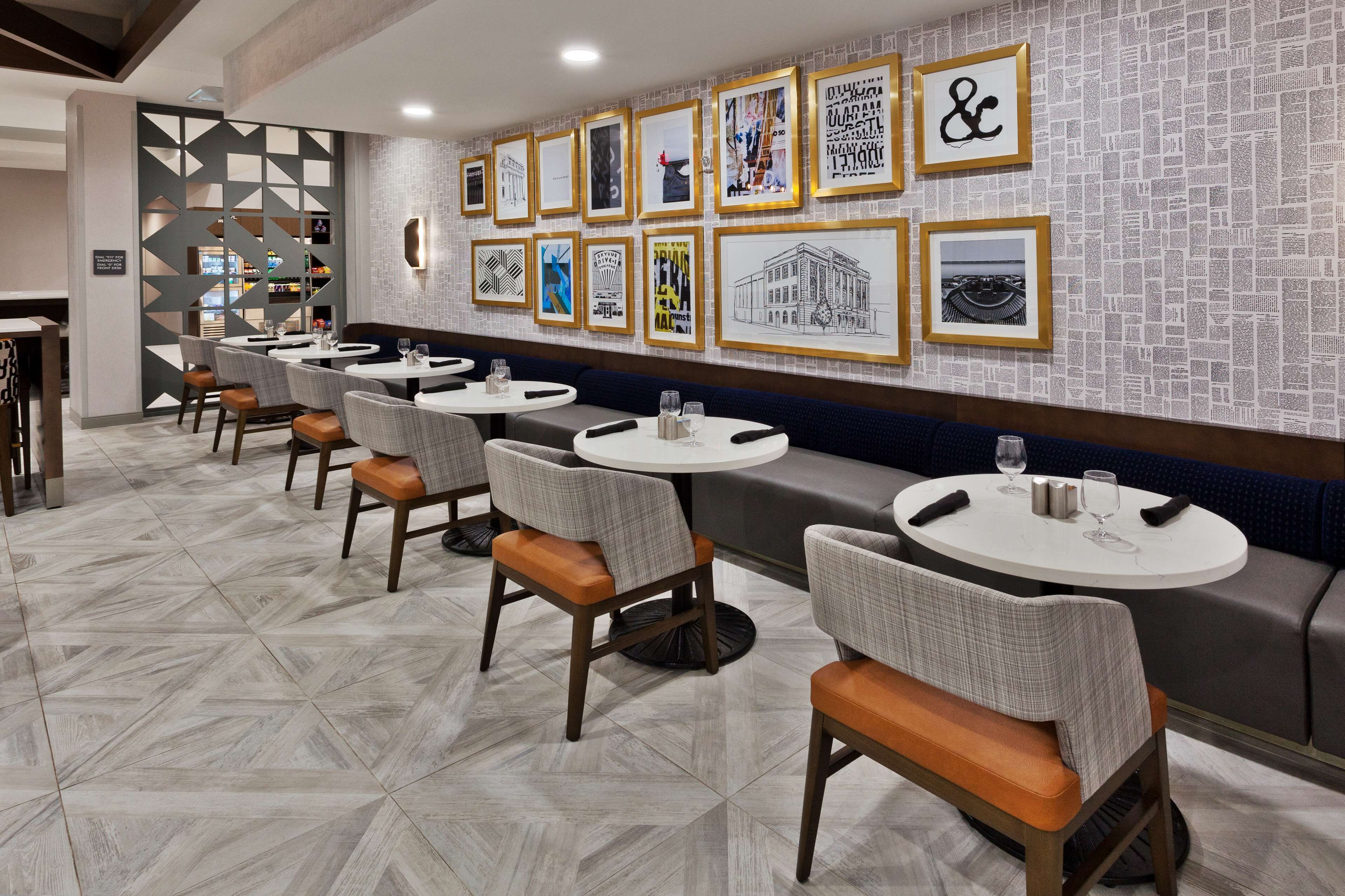 A restaurant with multiple round tables and chairs, a patterned floor, and a wall decorated with framed artwork.