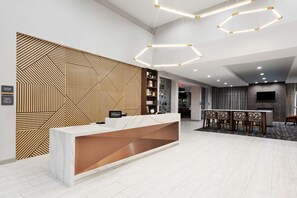 A modern hotel reception area with a geometric patterned wall, a marble reception desk, and a seating area with patterned chairs. - DoubleTree by Hilton Dothan, AL (Dothan)
