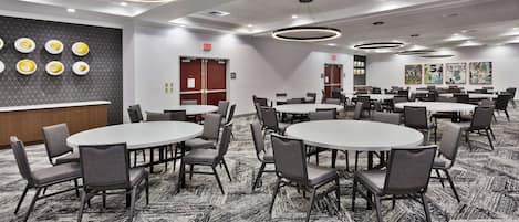 Une salle de conférence dotée de plusieurs tables rondes et de chaises, d’un tapis à motifs et de luminaires modernes.