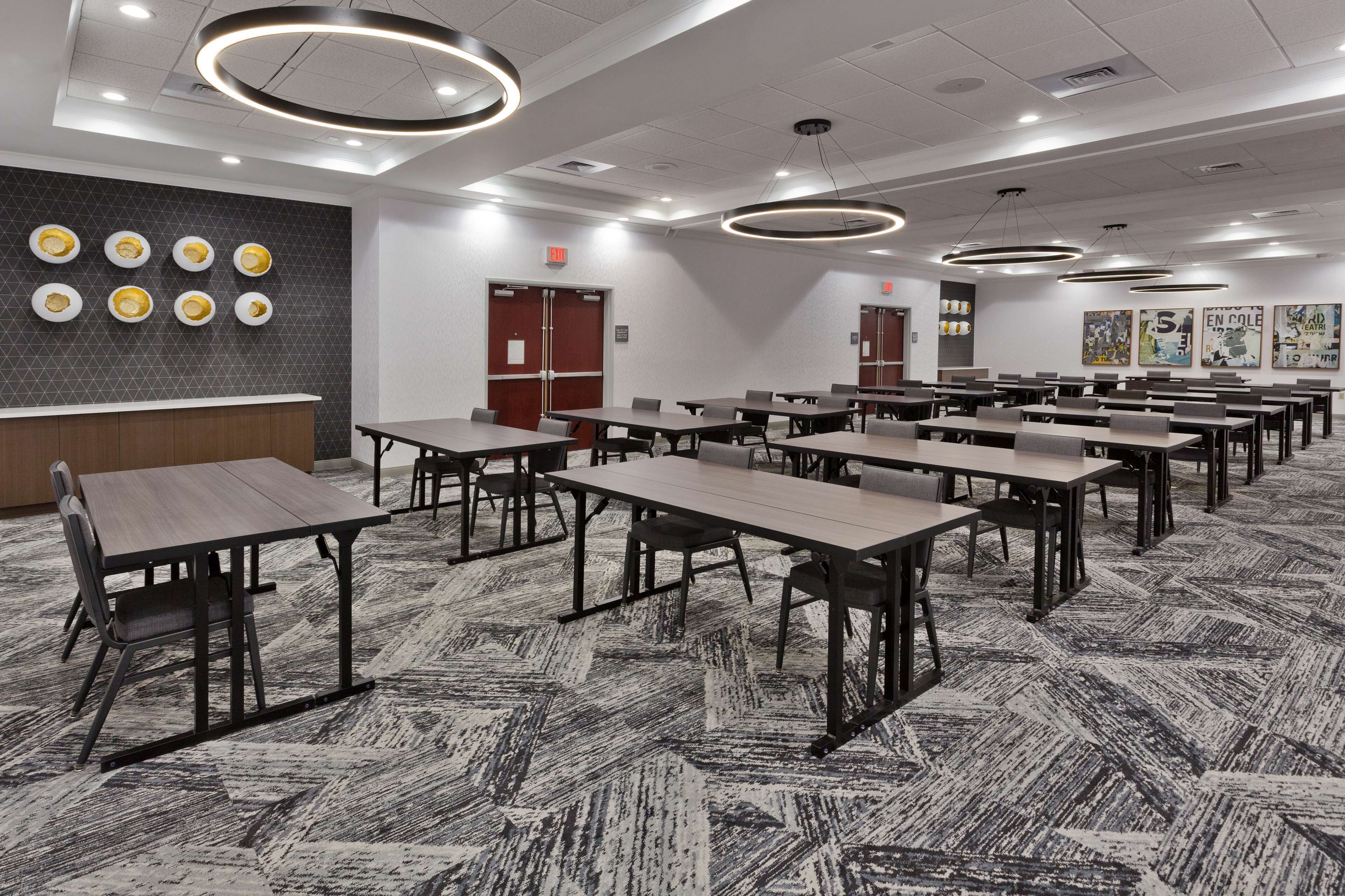 A conference room with multiple tables and chairs, a patterned carpet, and modern lighting fixtures.