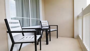A balcony with two white chairs and a table, a window with curtains, and a white railing.