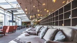 A modern lounge area with sofas and chairs, a wooden ceiling with hanging lights, and a large window providing natural light. - Torekov Hotell (Torekov)