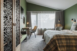 Habitación de hotel con cama, escritorio, silla y ventana con cortinas.