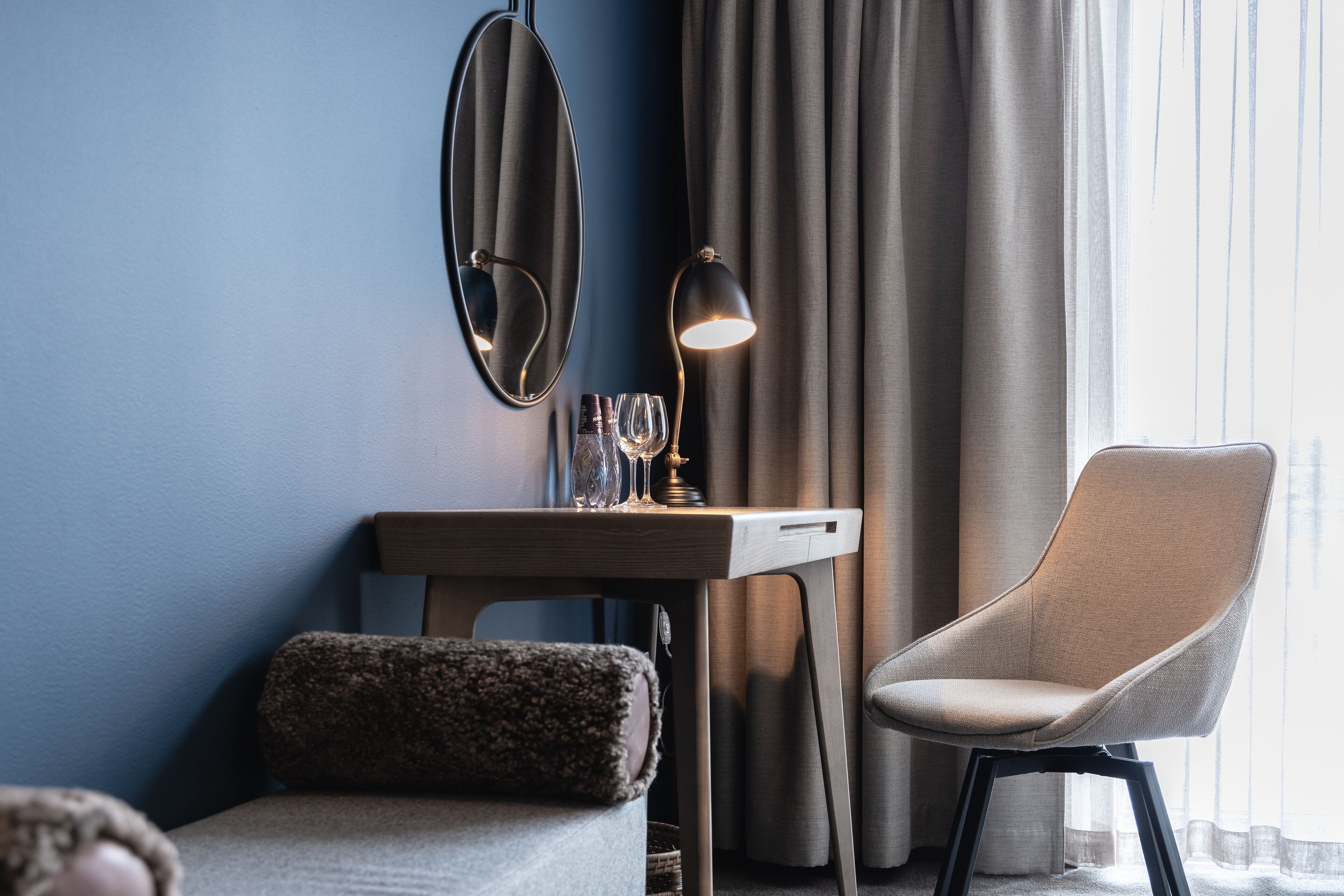 A hotel room with a bed, a desk with a lamp, a chair, and a mirror.