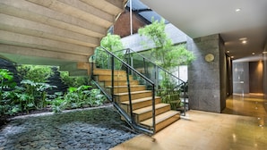 A modern staircase with glass railings, surrounded by lush indoor plants and a stone-tiled floor. - BOG Hotel  (Bogotá)