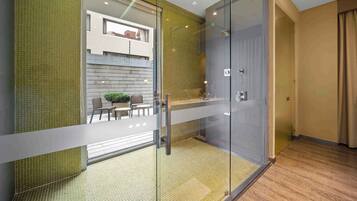 Un baño moderno con cabina de ducha de vidrio, suelo de madera y pared con azulejos verdes.