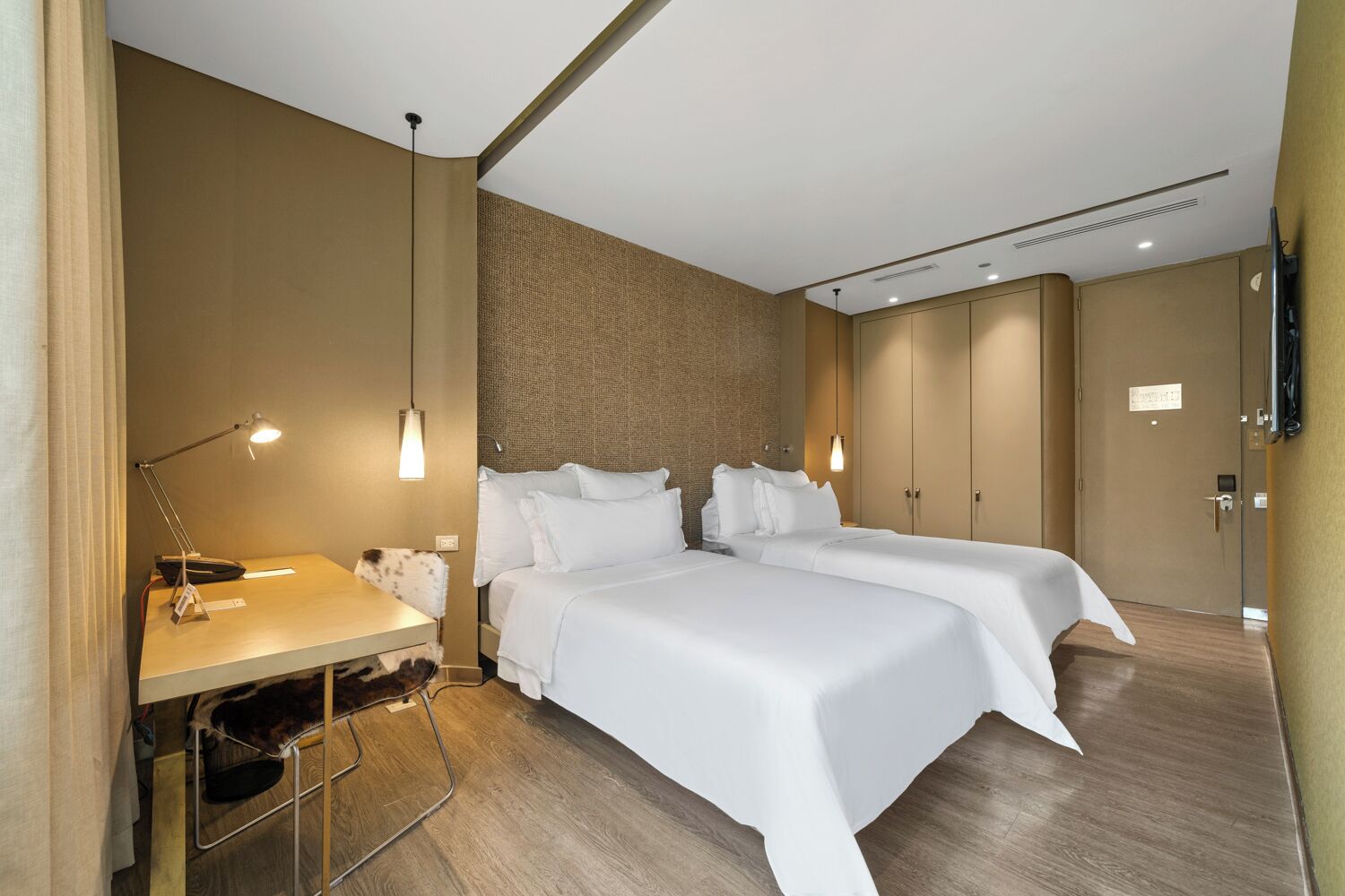 A hotel room with two beds, a desk with a chair, a flat-screen TV, and a wardrobe.