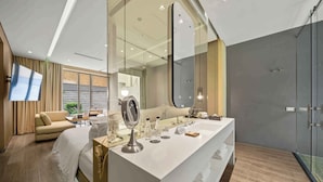 A modern hotel room with a large mirror, a vanity with toiletries, a sofa, and a glass shower enclosure. - BOG Hotel  (Bogotá)
