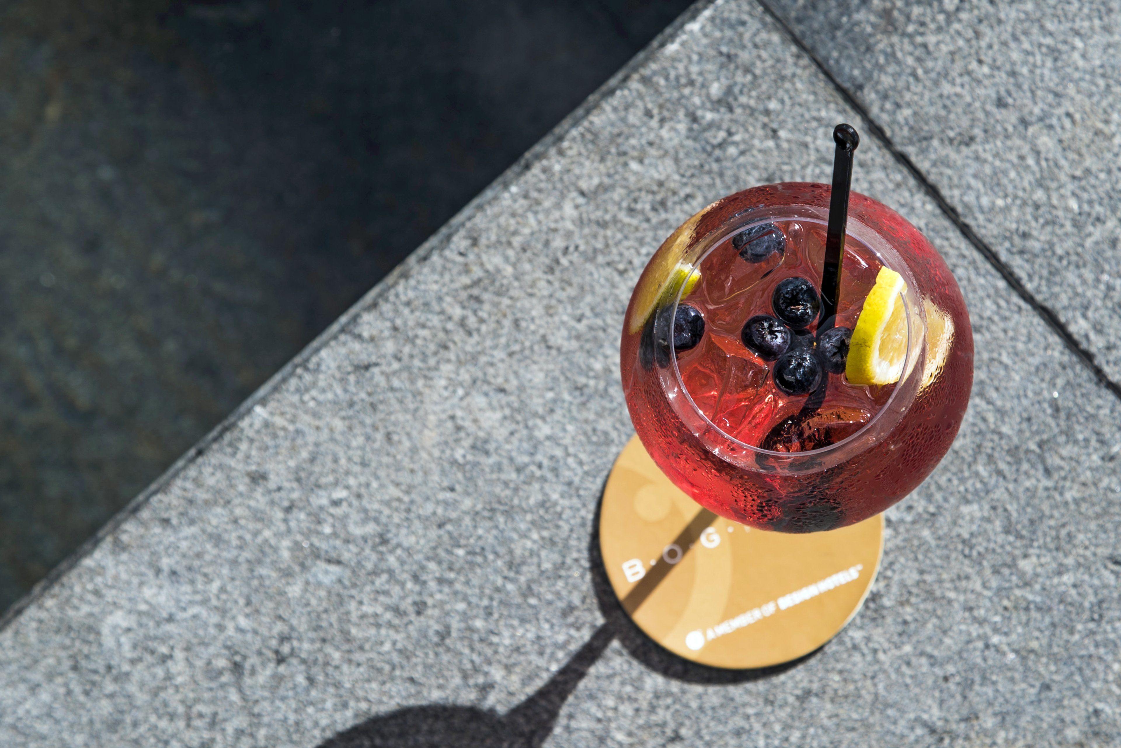 Une boisson servie avec une paille et une tranche de citron, posée sur un dessous de verre orné d’un texte.