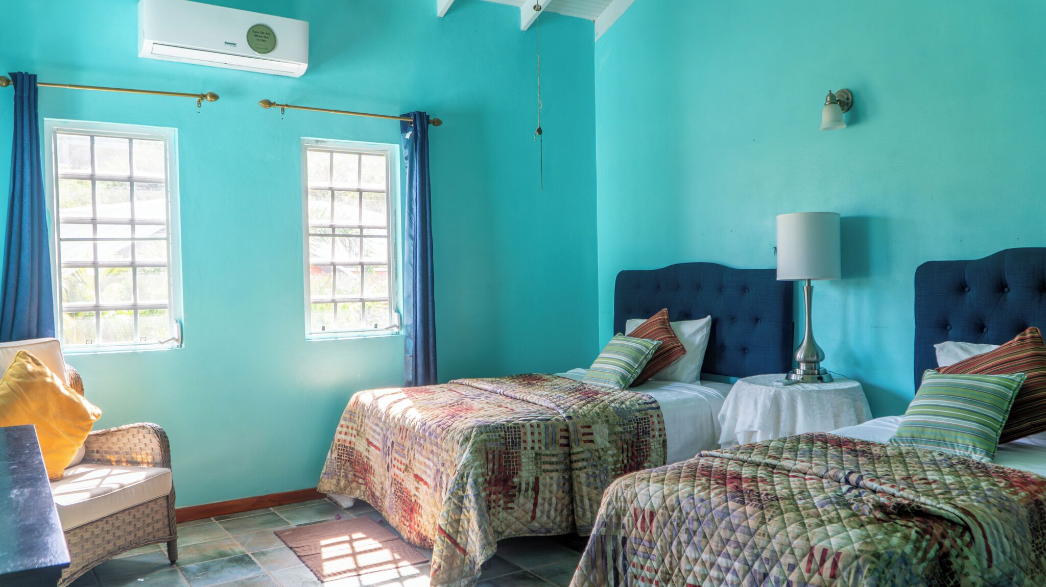 A room with two beds, a window, a chair, and an air conditioning unit.