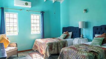 A room with two beds, a window, a chair, and an air conditioning unit.