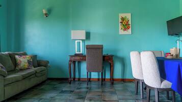 Una habitación con paredes verde azulado, un sofá, un escritorio con una silla, un televisor y una mesa con sillas.