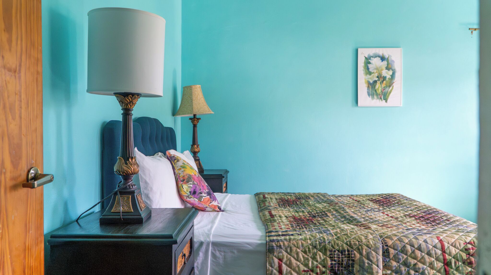 Een slaapkamer met een bed, twee nachtkastjes, een lamp, een schilderij aan de muur en een deur.