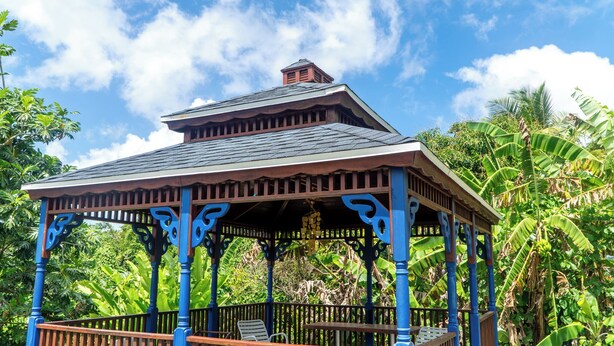 A gazebo with a sloped roof and ornate wooden railings, surrounded by lush tropical vegetation. - LambLion Holiday Apartments (Freemans Village)