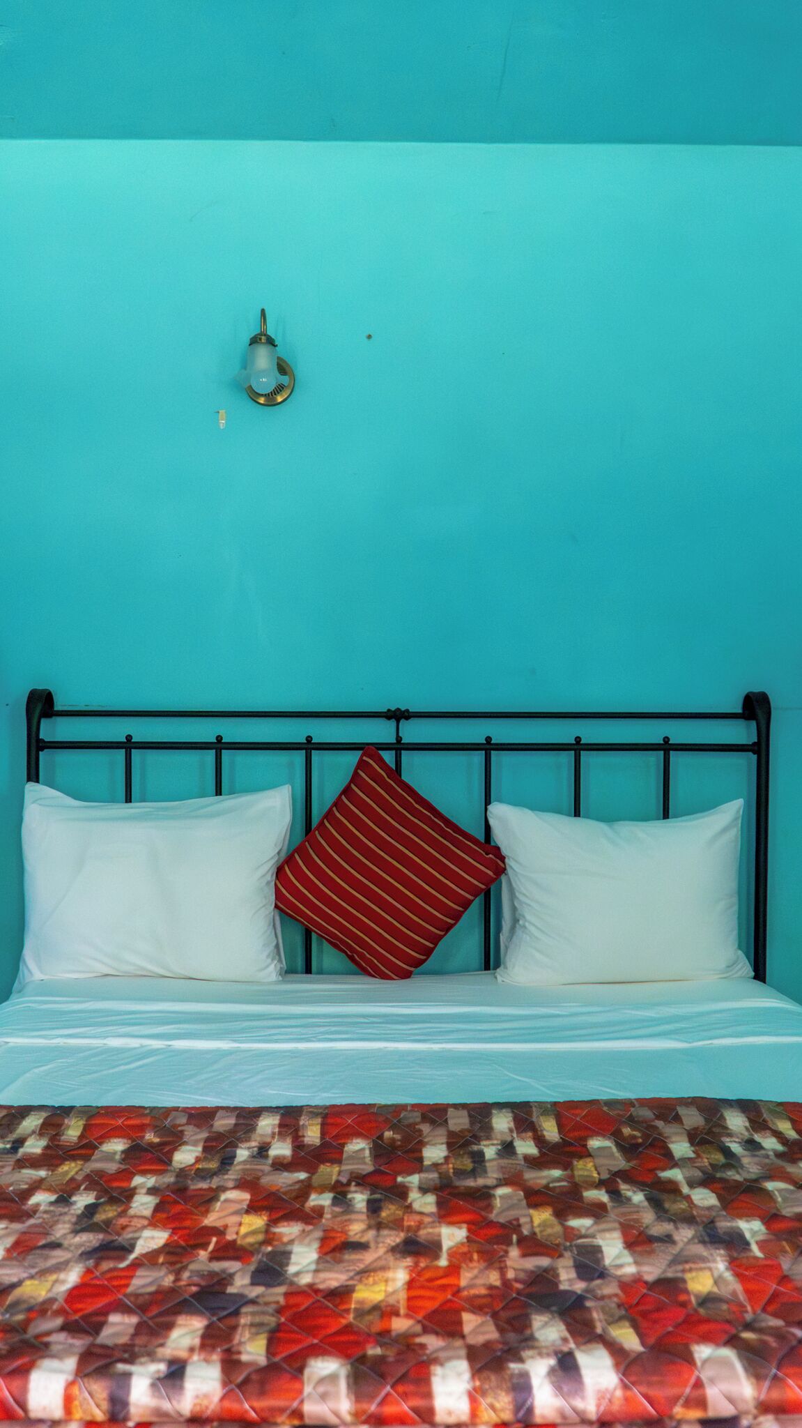 A bed with a metal frame, two white pillows, and a red striped pillow.
