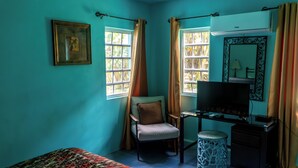 A room with teal walls, a bed, a chair, a TV, and a desk with a lamp. - LambLion Holiday Apartments (Freemans Village)