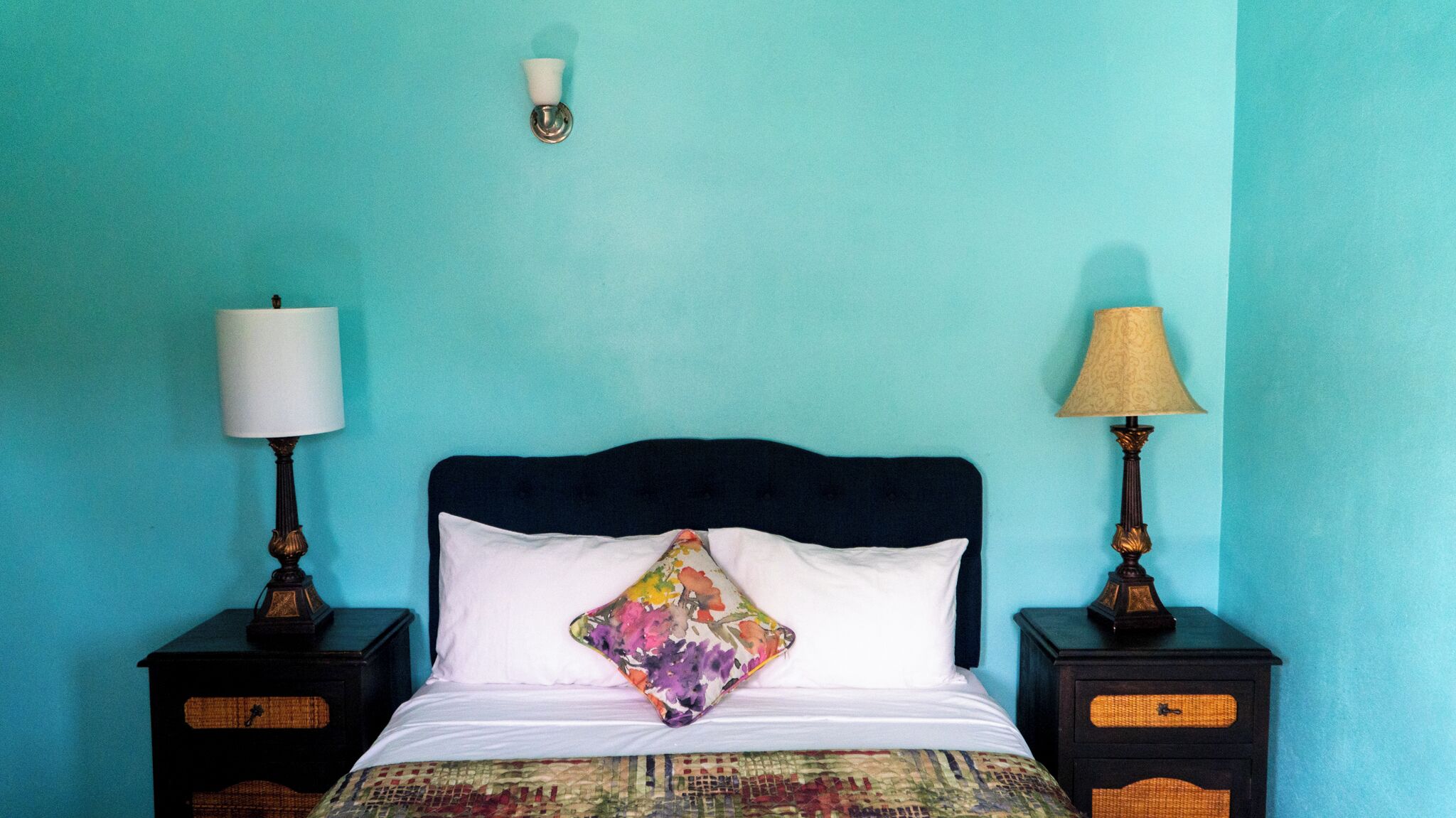 A bed with a floral pillow, two bedside tables with lamps, and a wall-mounted light fixture.