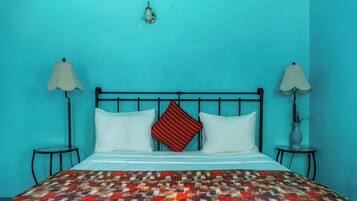 Uma cama com colcha estampada, um travesseiro listrado em vermelho e branco, e duas luminárias de cabeceira em ambos os lados.