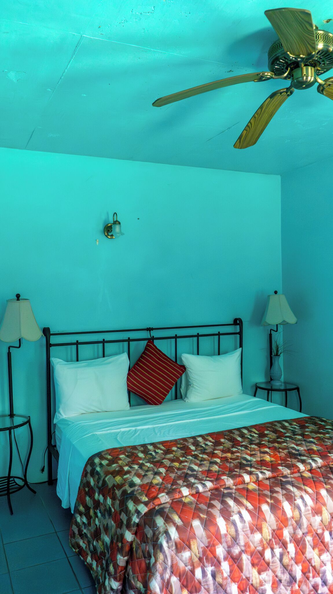 Een kamer met een bed, twee bedlampjes, een plafondventilator en een lichtschakelaar aan de muur.