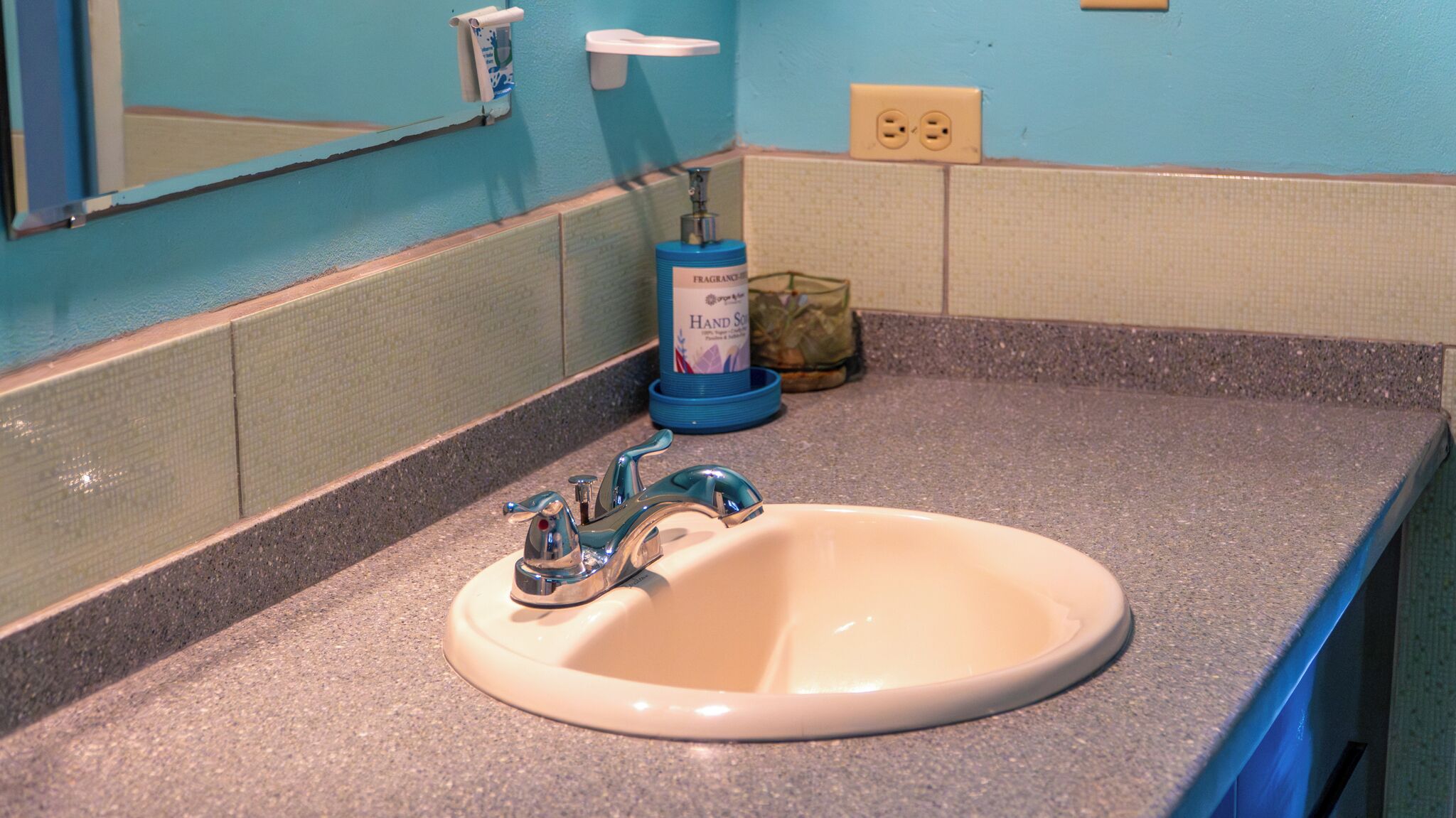 A bathroom sink with a blue faucet, a hand soap dispenser, and a mirror above it.