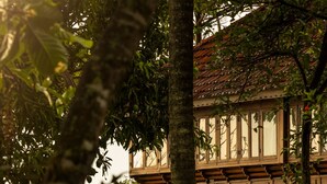 A traditional wooden house with a balcony, surrounded by lush greenery and a view of the water. - Coconut Lagoon Kumarakom- A CGH Earth Experience (Kottayam)