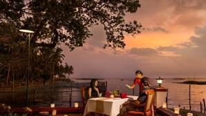 An outdoor dining area with a table set for two, surrounded by candles and a view of the sea. - Coconut Lagoon Kumarakom- A CGH Earth Experience (Kottayam)