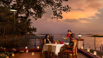 An outdoor dining area with a table set for two, surrounded by candles and a view of the sea.