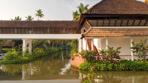 A traditional building with a tiled roof, a white facade, and a water body in front. - Coconut Lagoon Kumarakom- A CGH Earth Experience (Kottayam)