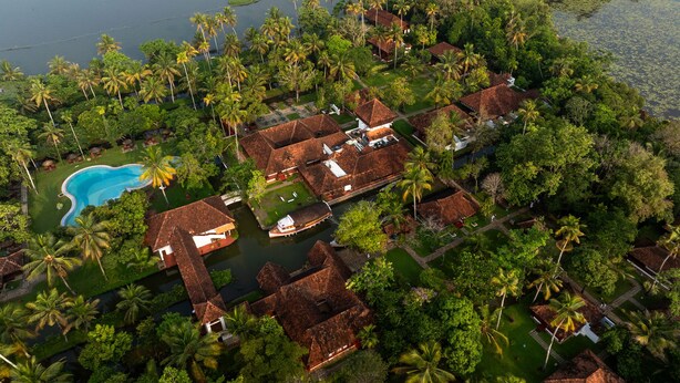 An aerial view of a resort with multiple bungalow-style buildings, a swimming pool, and a body of water. - Coconut Lagoon Kumarakom- A CGH Earth Experience (Kottayam)