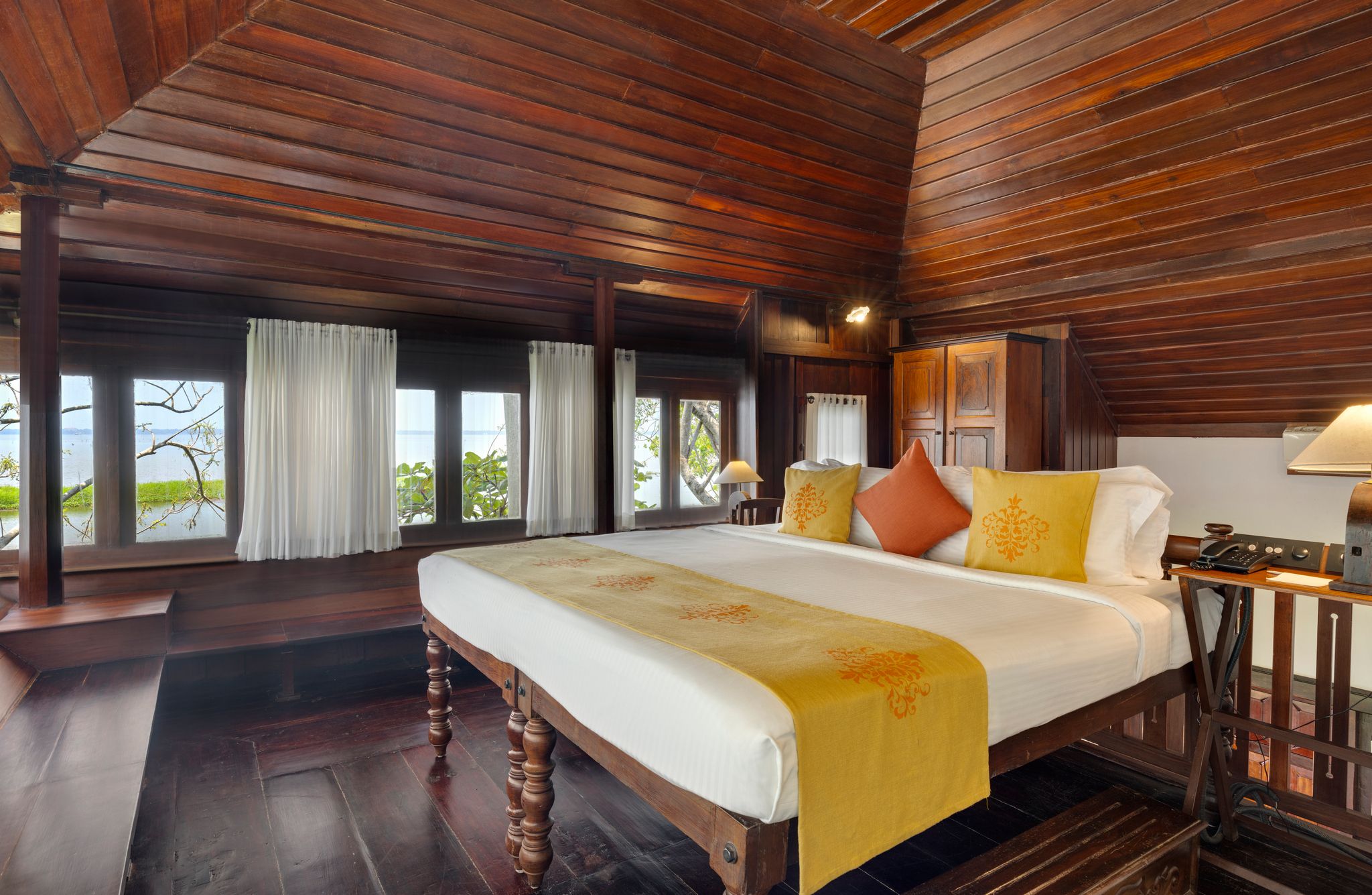 A wooden-paneled room with a large bed, a desk, and windows with curtains.