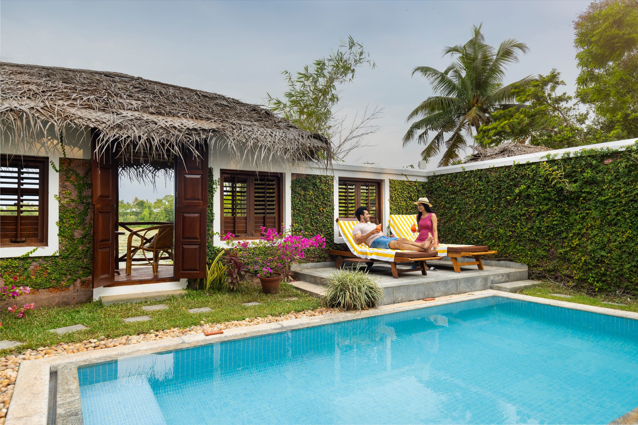 A poolside area with a thatched-roof structure, a pool, and a garden with potted plants.
