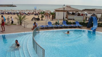Relax by the oceanfront pool surrounded by lounge chairs and umbrellas, with a lifeguard on duty.