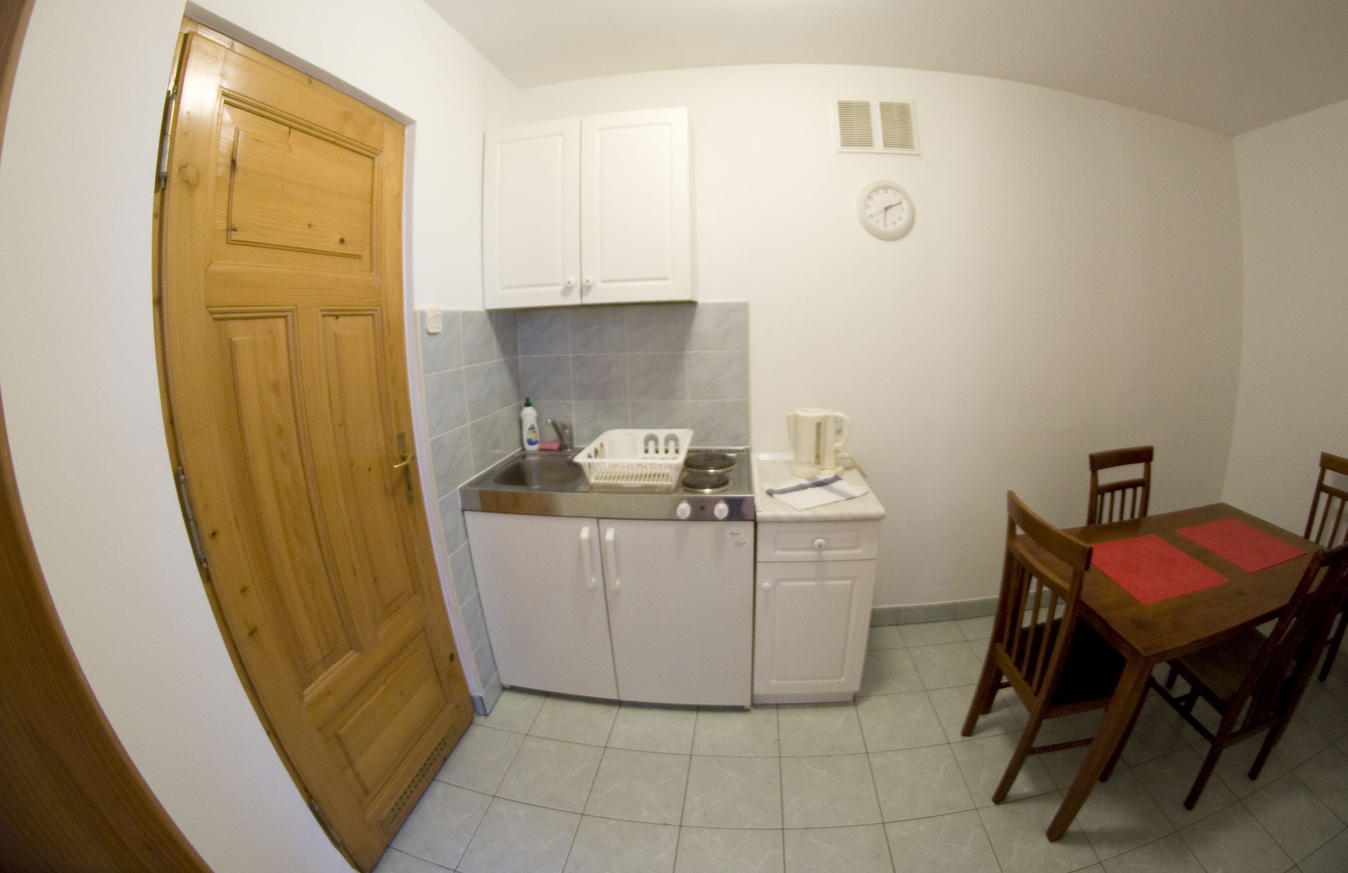 A compact kitchen with a wooden door, white cabinets, a stove, and a dining table with chairs.