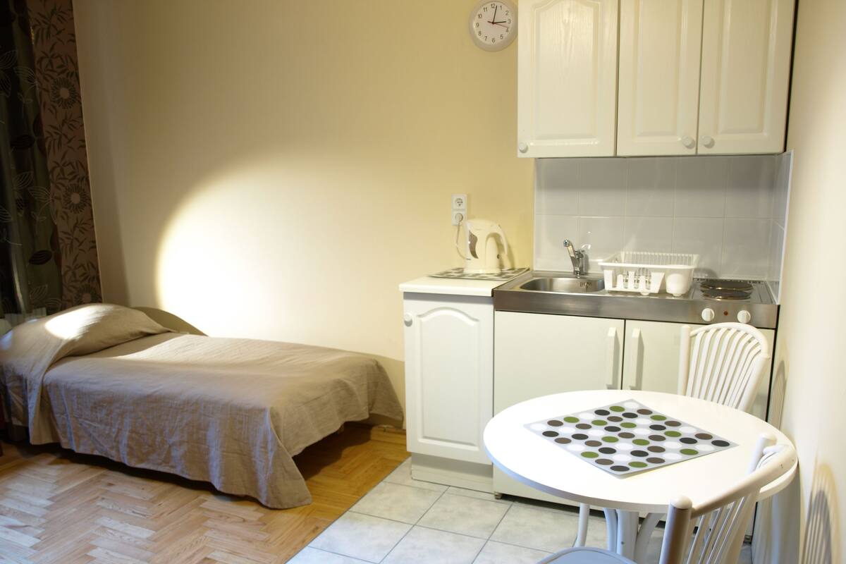 A small, compact room with a bed, a kitchenette, and a dining area.