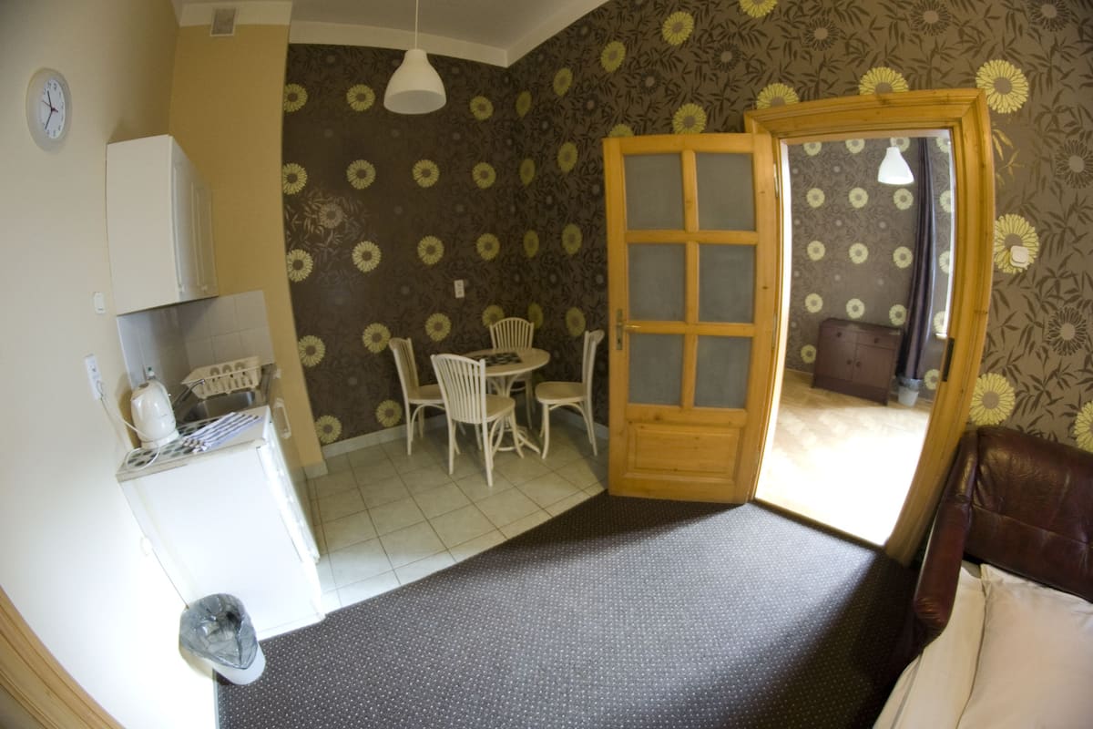 A compact room with a dining area, a small kitchen, and a door leading to another room.