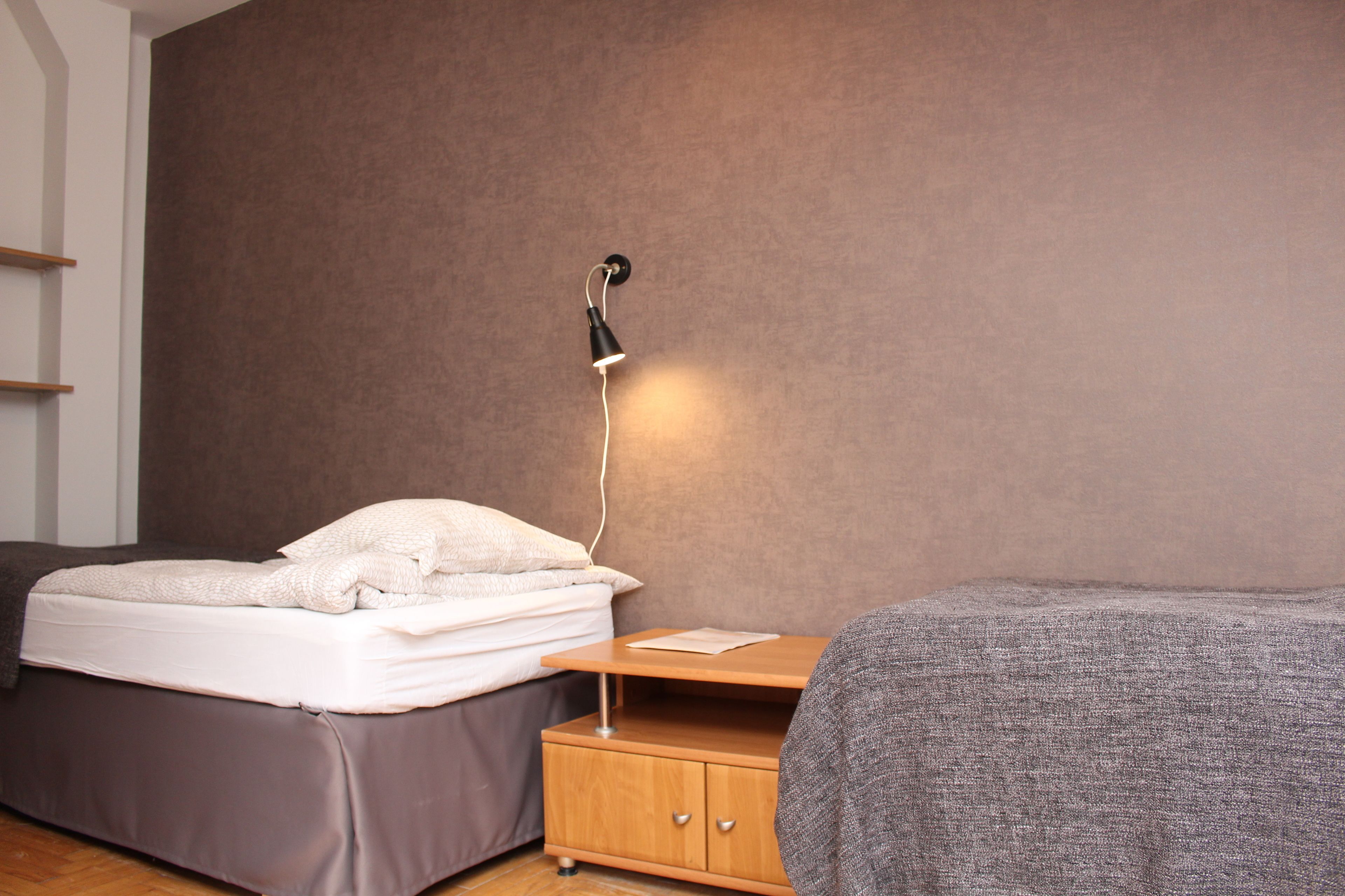 A bedroom with a bed, a bedside table, and a wall-mounted lamp.