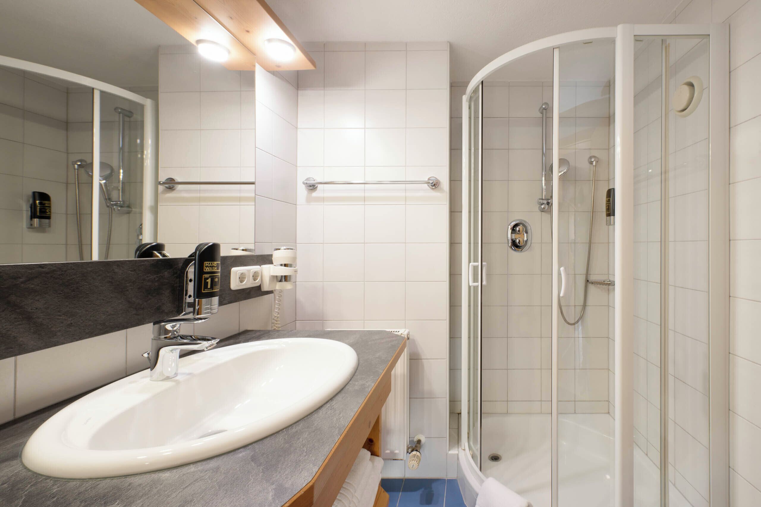 Une salle de bain moderne avec un lavabo blanc, une douche en verre et un meuble-lavabo en bois.