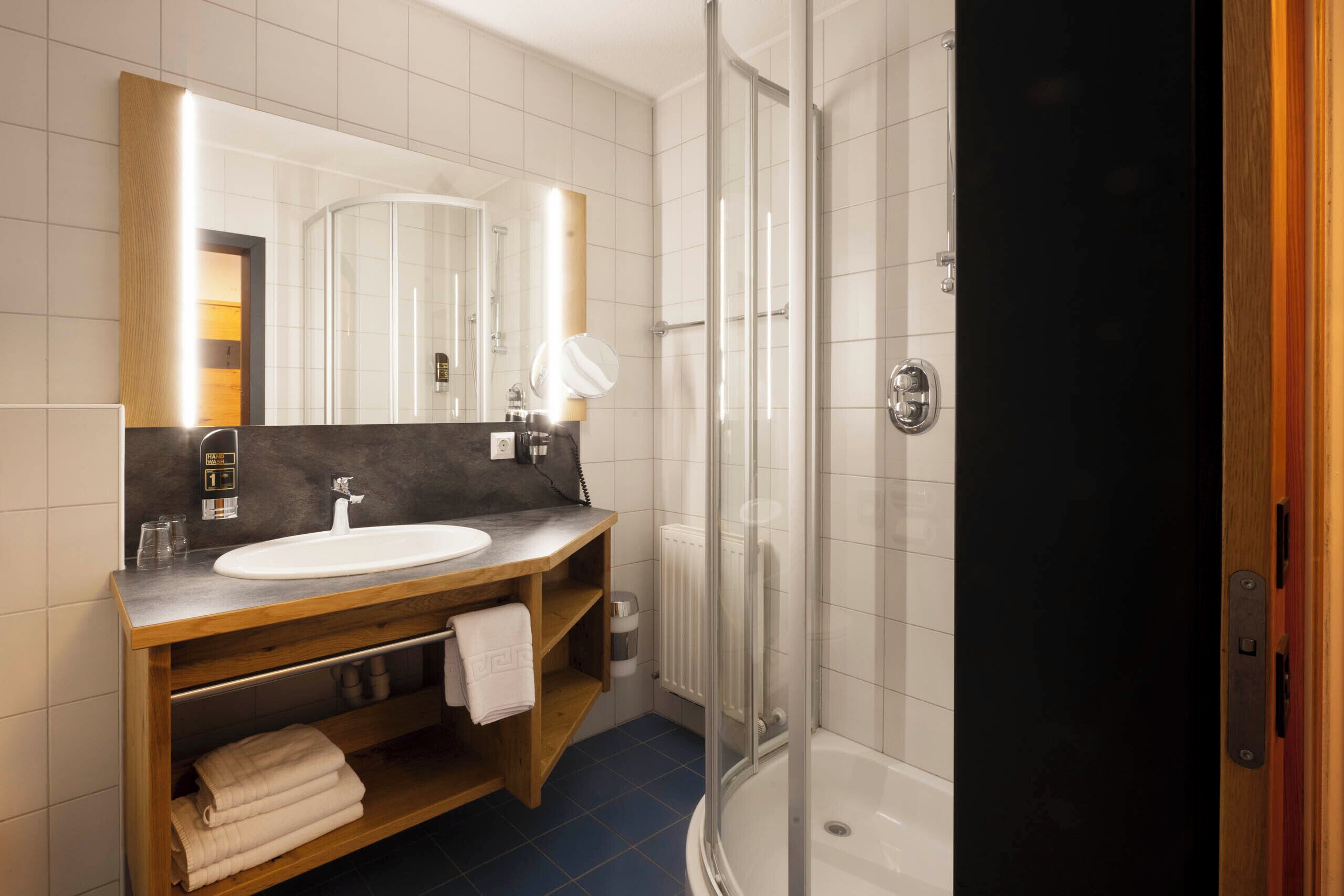 Un baño moderno con lavamanos, espejo, toallero y cabina de ducha de vidrio.