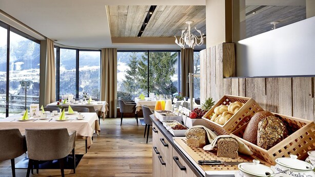 Un bufé de desayuno con panes y pasteles variados, una estación de café y vistas a montañas nevadas.