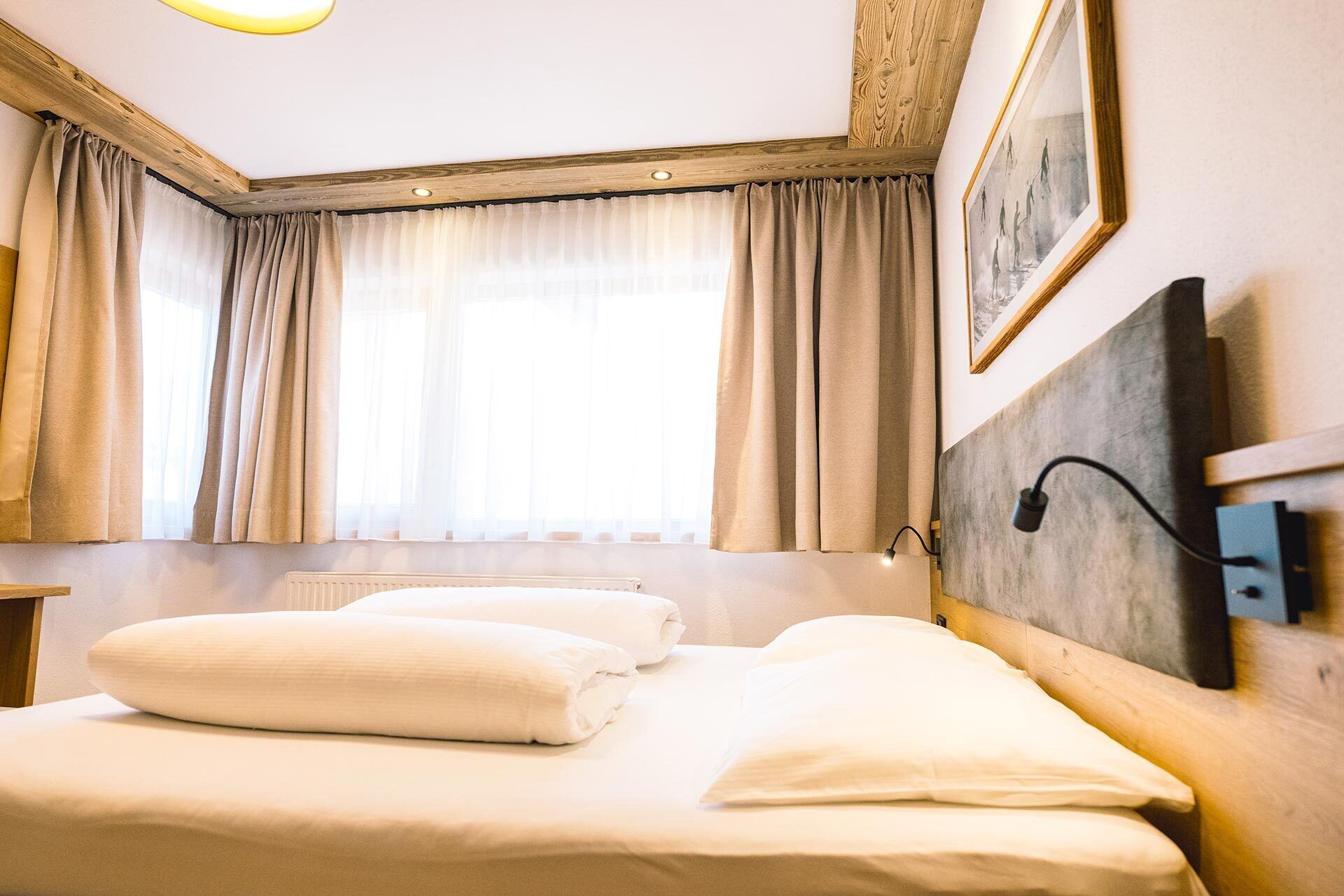 Habitación de hotel con una cama, una mesita de noche, una lámpara, una ventana con cortinas y un cuadro en la pared.