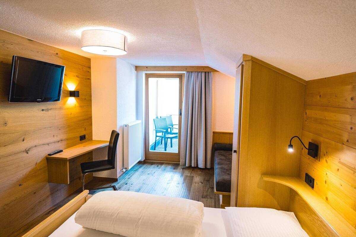 Habitación de hotel con cama, escritorio, silla, televisión y ventana con cortinas.