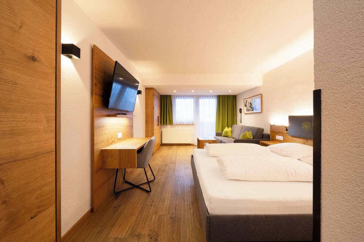 Habitación de hotel con cama, escritorio, silla, televisor, ventana con cortinas e imagen en la pared.
