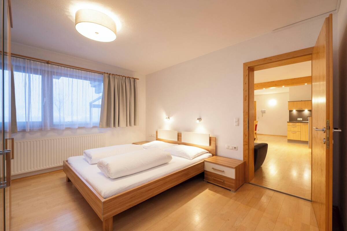 Un hotel moderno con cama de madera, mesitas de noche, armario empotrado y vistas a la cocina contigua.