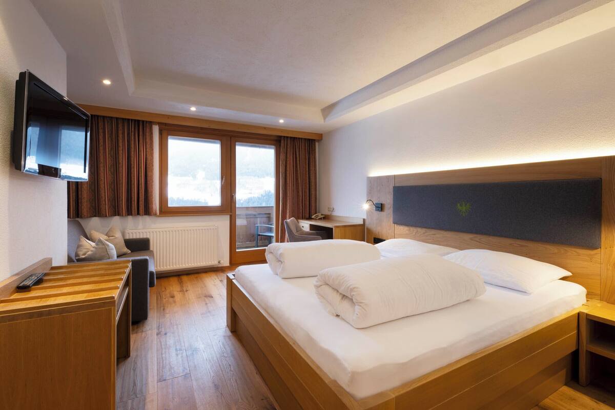 Habitación de hotel con cama, escritorio, silla, televisor y ventana con cortinas.