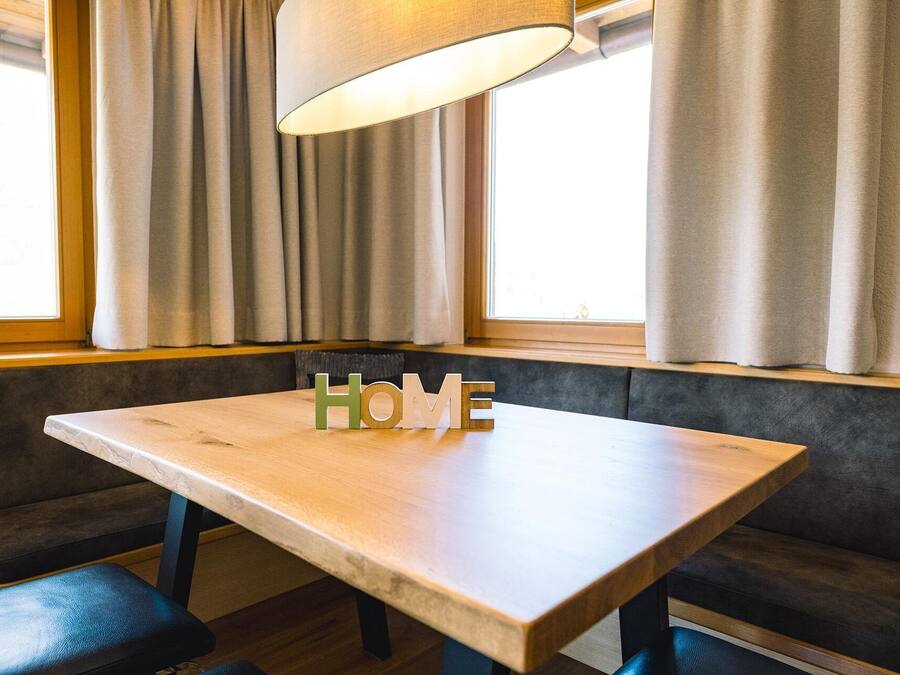 A wooden table with 'HOME' letters in the center, a bench, and a window with curtains.