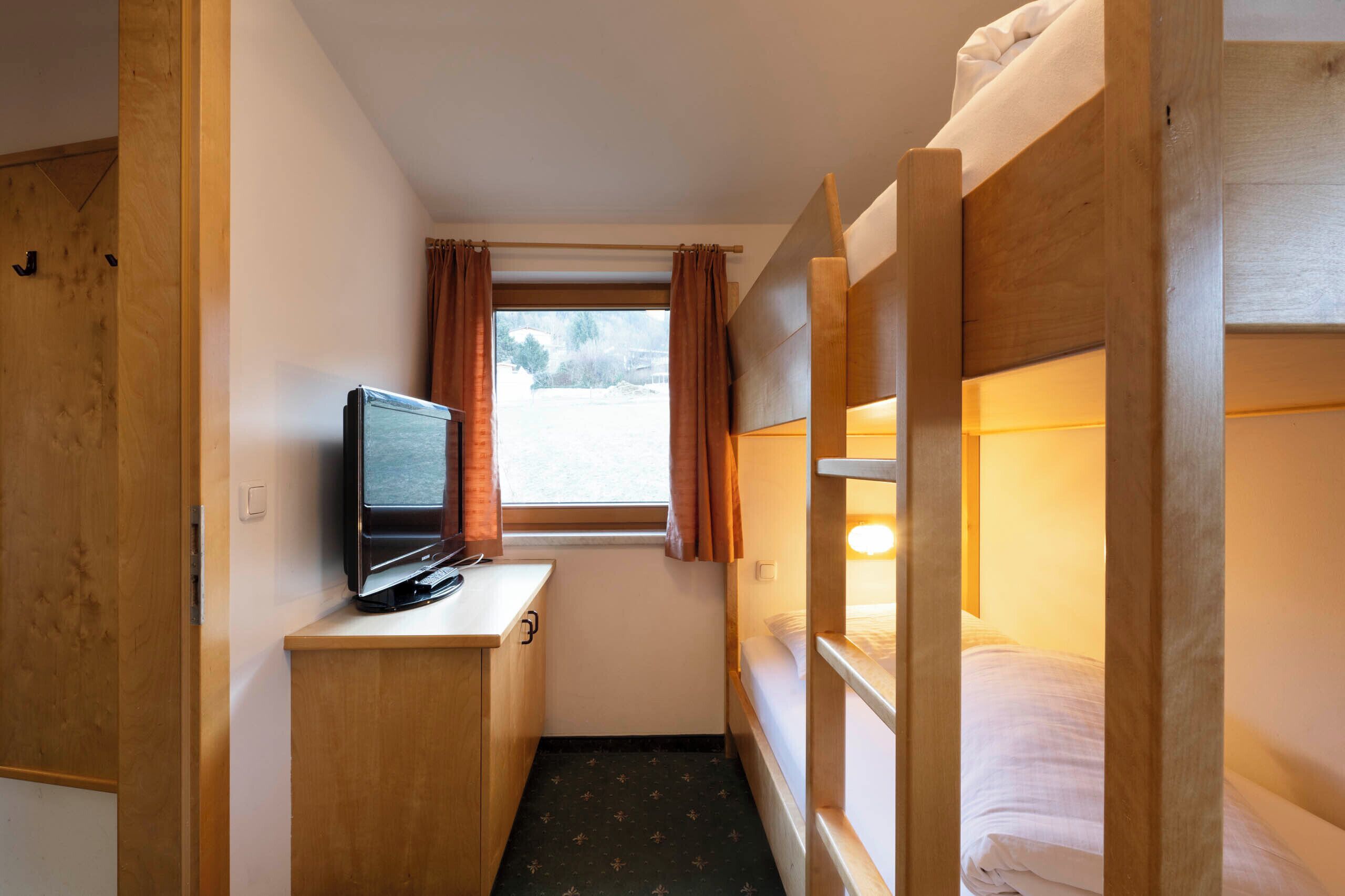 Una habitación compacta con literas, un escritorio pequeño con televisor y una ventana con cortinas.