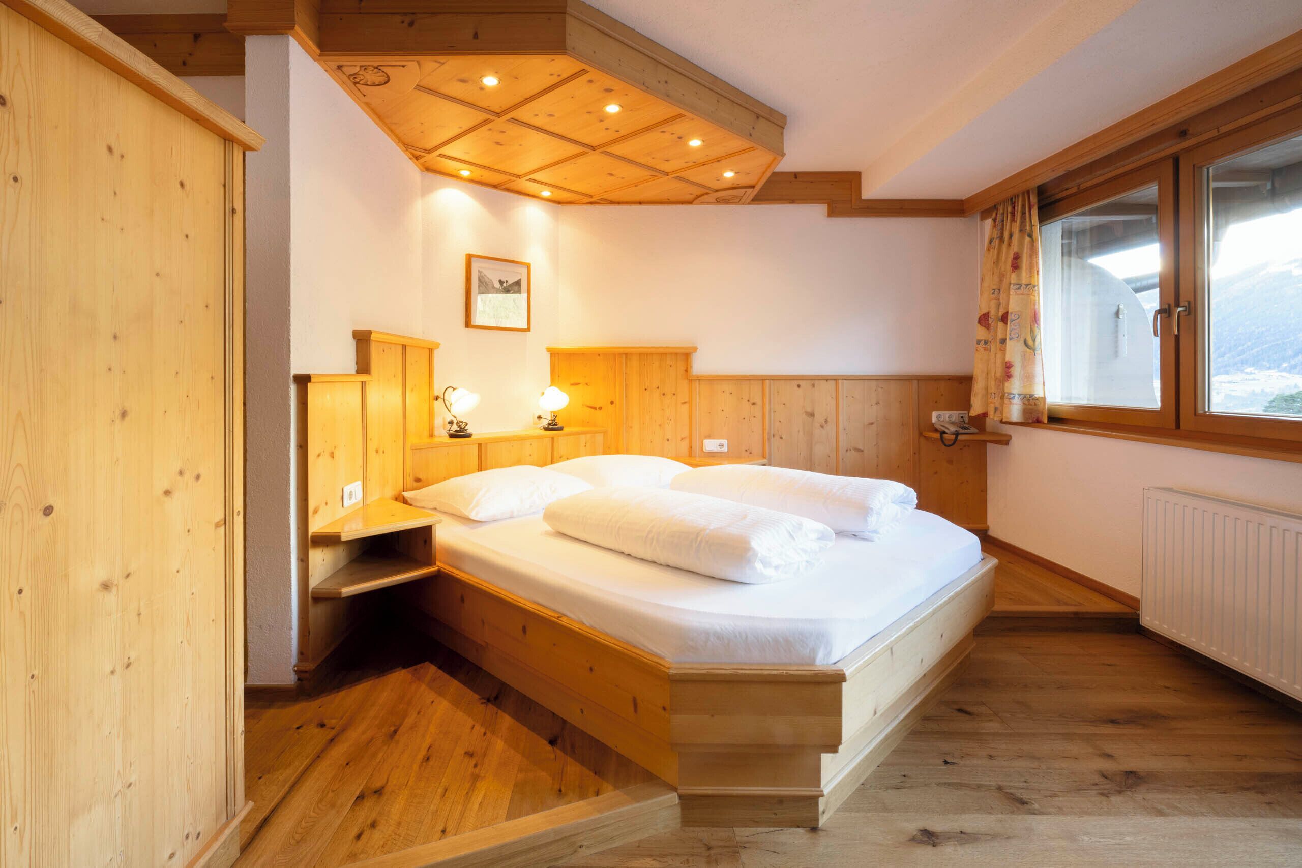 A wooden bedroom with a bed, bedside lamps, a window with curtains, and a framed picture on the wall.