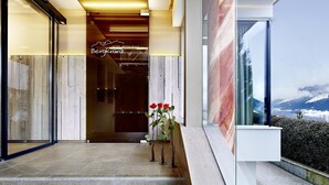 Entrada de un hotel con fachada de madera, un letrero que dice 'Hotel Restaurant Bergkranz' y vistas de montañas nevadas.